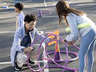 A man outside is assisted by a woman building an enclosure with purple hula hoops. 