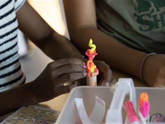 Two hands construct a fluorescent figurine a on a stick. 