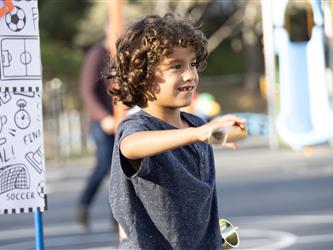 A boy with curly brown hair holds a stick and smiles.
