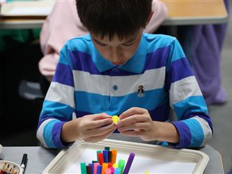 A boy in a striped shirt puts two pieces of clay together. 