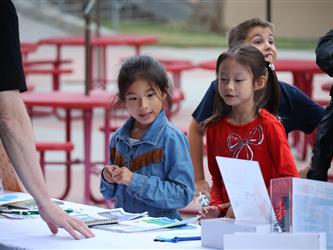 Two girls sign up for a prize at a table. 