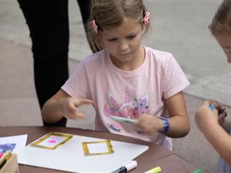 A girl in a pink shirt builds a picture frame on a piece of paper.