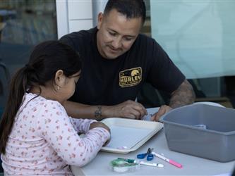 A man leans over to help a child work on a project. 
