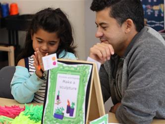 A man looks on as a girl colors a piece of paper. 