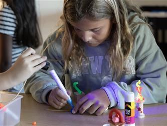 A girl in a green sweater colors a paper with a marker.