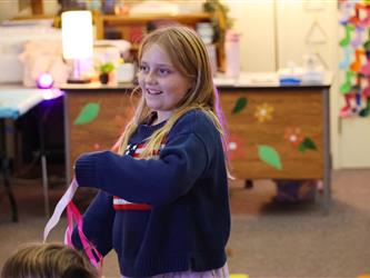 A girl with a blue sweatshirt holds a colorful ribbon. 