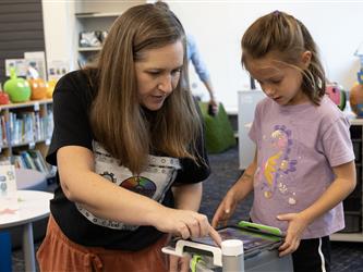 A woman helps a girl on a tablet