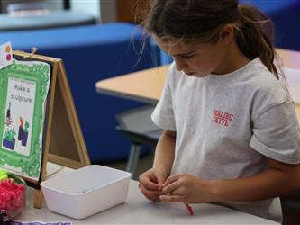 A girl ties a ribbon at a white table. 