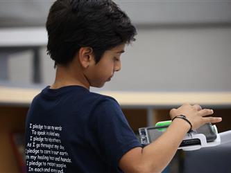 A boy with a blue shirt types on a tablet.
