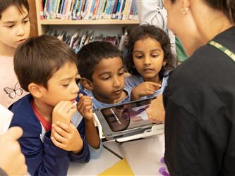 A teacher shows three children an image on a tablet. 