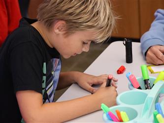A boy colors a piece of paper with a marker. 